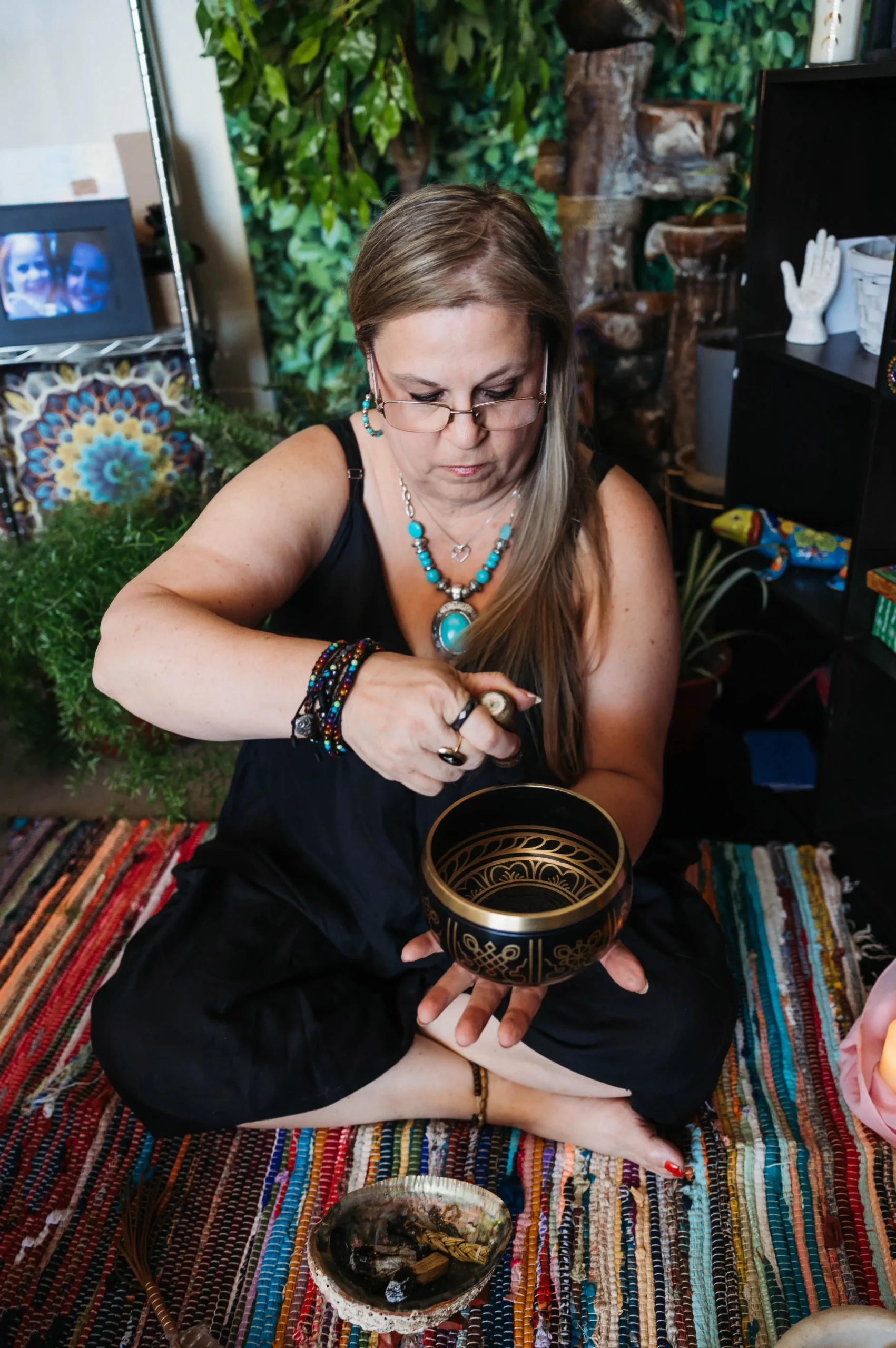 A woman sits on the floor, enjoying a bowl of food, with a relaxed expression and a cozy atmosphere around her.